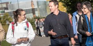 A close up of Mark Turin talking to Linguistics student Paris, while walking in front of the Musqueam sʔi:ɬqəy̓ qeqən